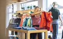 Junge Frau in Sportkleidung schaut sich eine rote Regenjacke im Sortiment an | © Bergbahnen Flumserberg AG